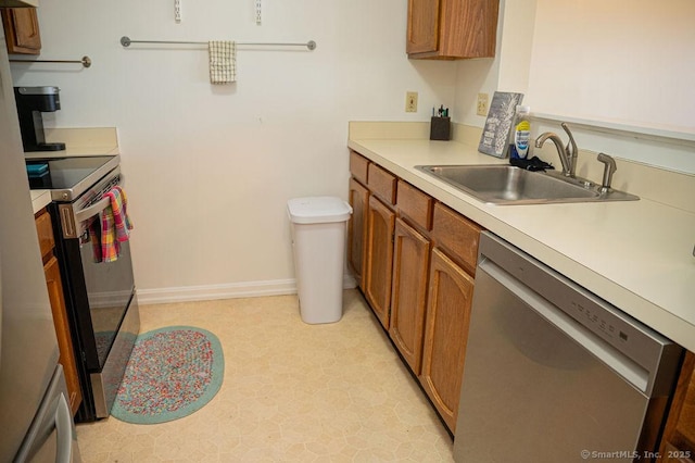 kitchen featuring baseboards, light countertops, brown cabinets, stainless steel appliances, and a sink