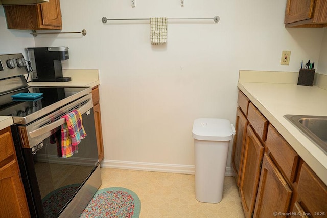 kitchen with electric range, brown cabinets, baseboards, and light countertops