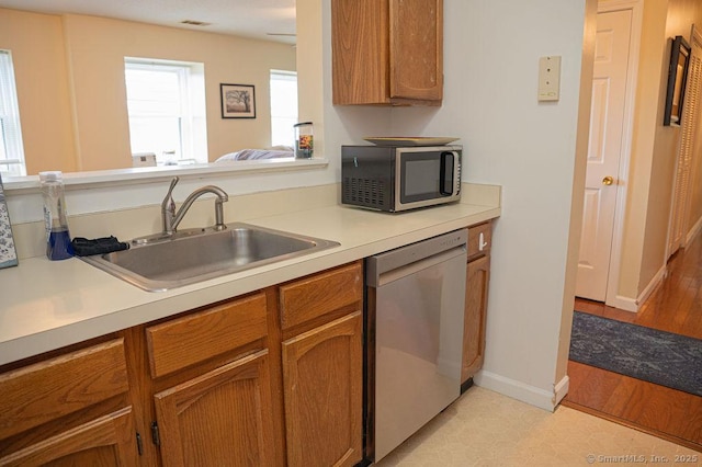 kitchen with brown cabinets, a sink, stainless steel appliances, light countertops, and baseboards