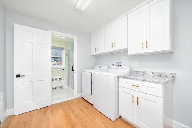 laundry room featuring radiator, baseboards, washing machine and dryer, light wood-style floors, and cabinet space