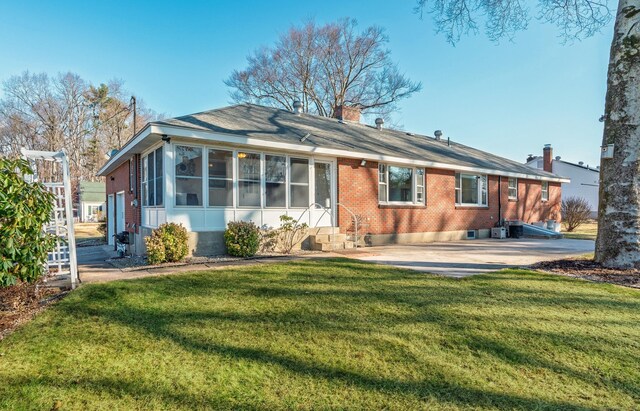 back of house with entry steps, a yard, a sunroom, brick siding, and a chimney