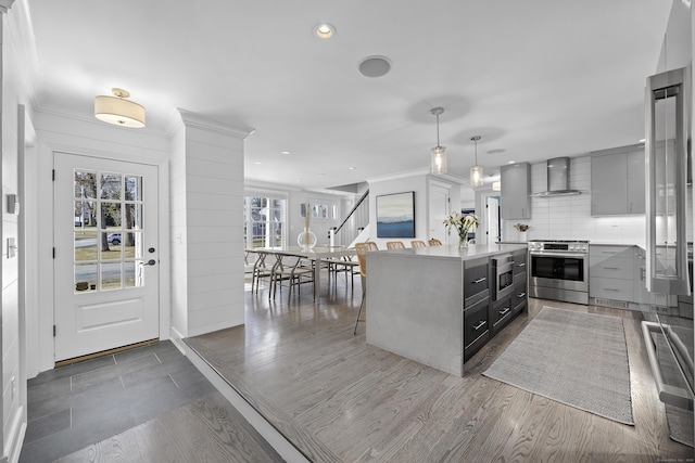 kitchen with crown molding, light countertops, appliances with stainless steel finishes, wall chimney exhaust hood, and dark wood-style flooring