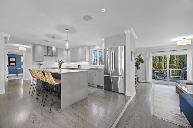 kitchen with a breakfast bar, a sink, freestanding refrigerator, wall chimney exhaust hood, and decorative backsplash