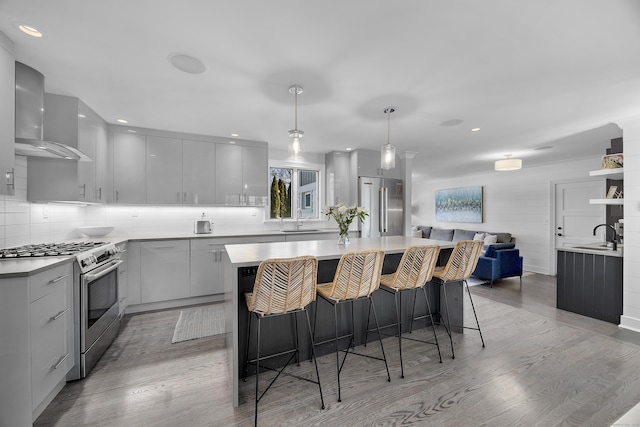 kitchen featuring wall chimney range hood, gray cabinets, light wood-style flooring, stainless steel appliances, and a sink