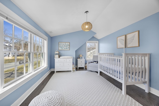 bedroom with dark wood finished floors, a crib, baseboards, and lofted ceiling