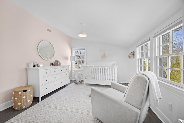 bedroom with a crib, vaulted ceiling, visible vents, and dark wood-type flooring