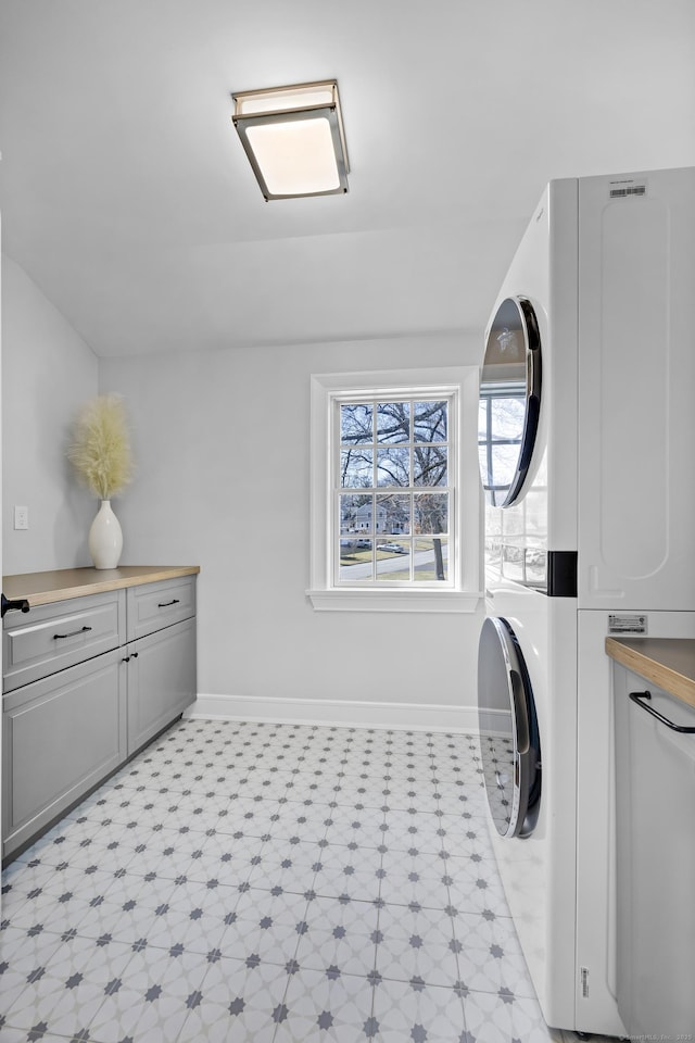 washroom with baseboards, light floors, cabinet space, and stacked washing maching and dryer