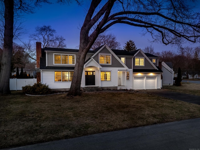 view of front facade featuring a front lawn, aphalt driveway, fence, board and batten siding, and a chimney