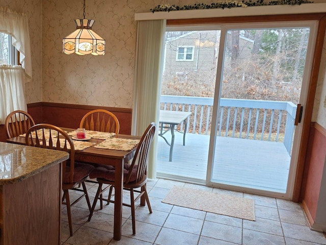 dining space featuring wallpapered walls, light tile patterned flooring, a healthy amount of sunlight, and wainscoting