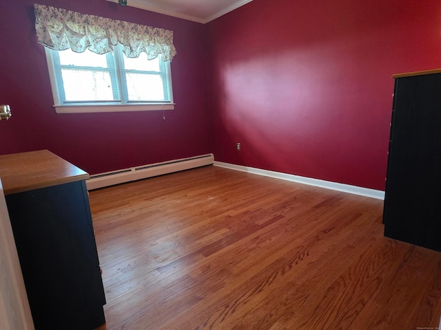 spare room featuring a baseboard radiator, baseboards, wood finished floors, and crown molding