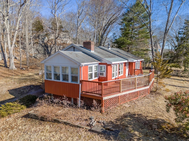 view of front of home with solar panels, a wooden deck, roof with shingles, and a chimney