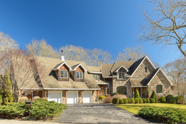 view of front facade with a chimney, a front lawn, a garage, stone siding, and aphalt driveway