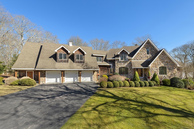 view of front facade with aphalt driveway, a front yard, a chimney, stone siding, and an attached garage