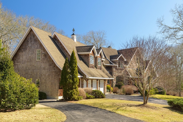 view of front of home featuring a front yard, a chimney, driveway, and a shingled roof