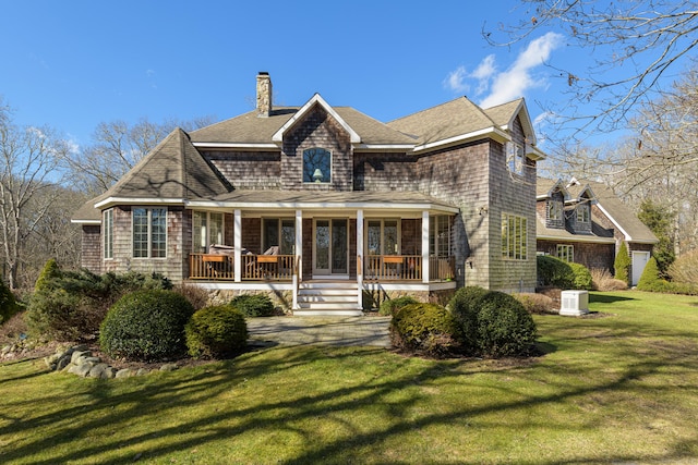 back of property featuring covered porch, a chimney, a yard, and roof with shingles