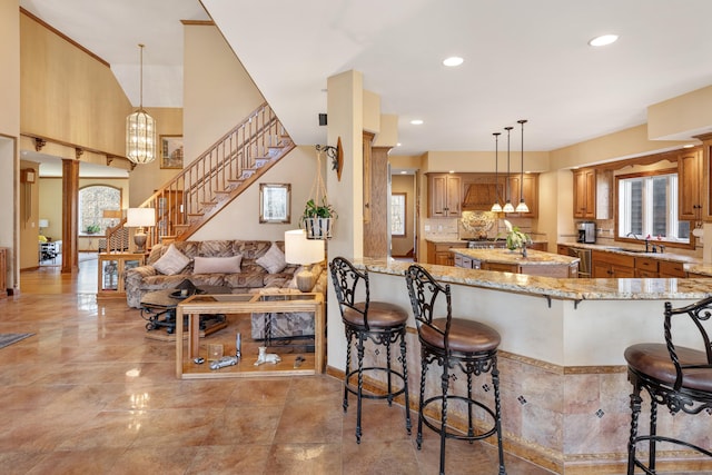 kitchen featuring hanging light fixtures, light stone countertops, a kitchen bar, and a sink