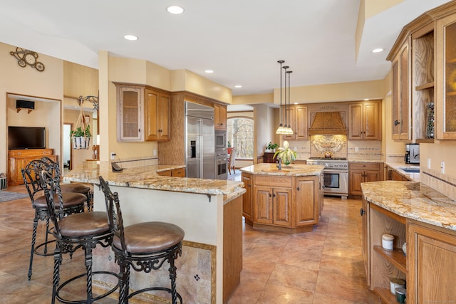 kitchen featuring light stone counters, a peninsula, custom exhaust hood, built in appliances, and a kitchen breakfast bar