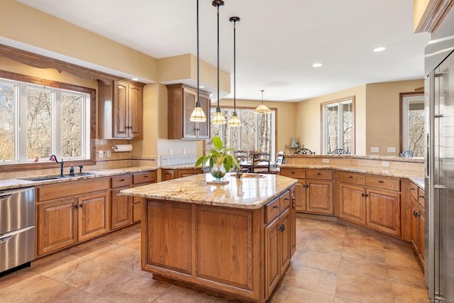 kitchen with a center island, light stone countertops, hanging light fixtures, brown cabinetry, and a sink