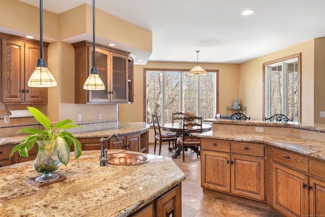 kitchen with brown cabinets, pendant lighting, light stone countertops, and a sink