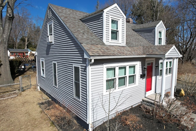 cape cod house featuring roof with shingles and fence