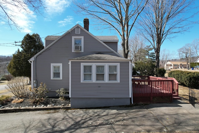 view of side of home featuring a wooden deck, roof with shingles, and a chimney