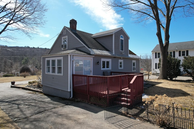 rear view of house featuring a wooden deck, fence, roof with shingles, and a chimney