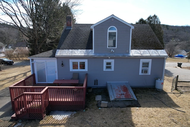 back of house with a wooden deck, a chimney, and roof with shingles