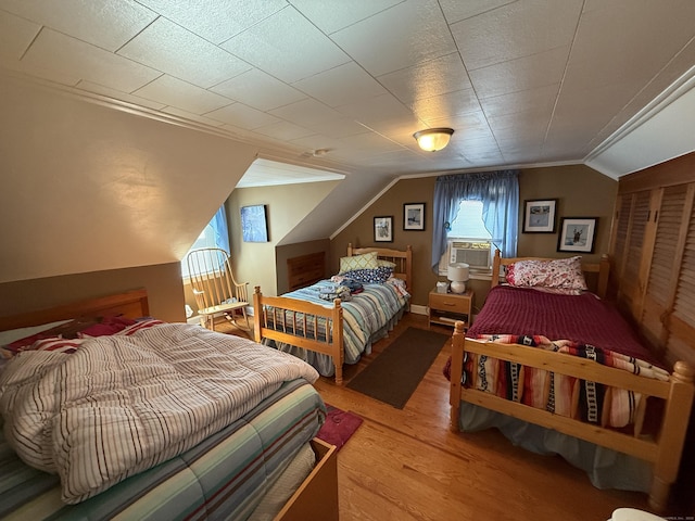 bedroom with wood finished floors, crown molding, and vaulted ceiling