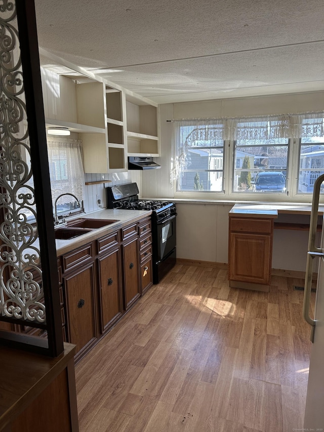 kitchen featuring black gas range oven, open shelves, under cabinet range hood, light wood-style floors, and a sink