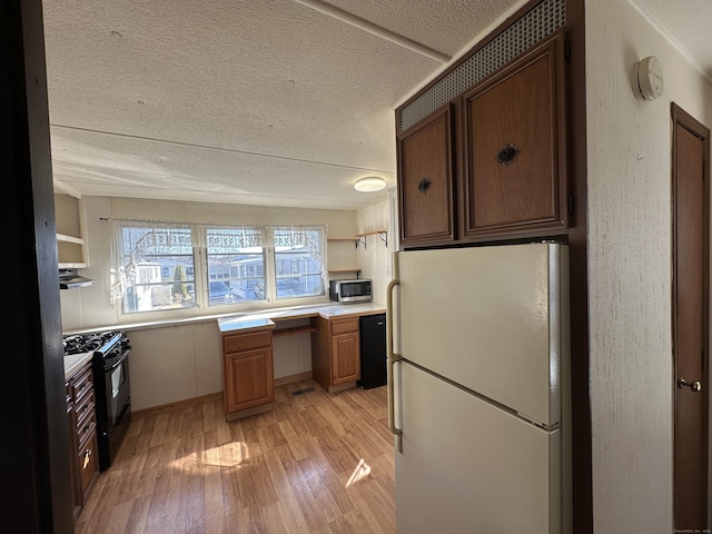 kitchen with freestanding refrigerator, built in desk, black range with gas stovetop, stainless steel microwave, and light wood-type flooring