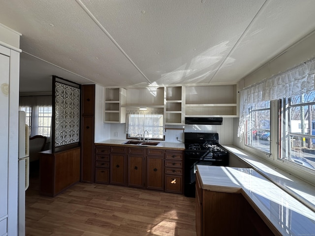 kitchen featuring black gas range oven, open shelves, exhaust hood, wood finished floors, and a sink