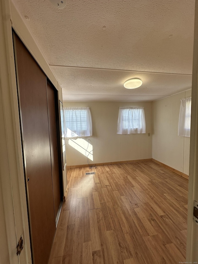 interior space with baseboards, visible vents, a textured ceiling, and light wood-style floors