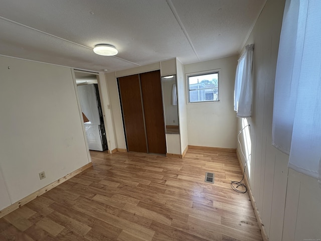 unfurnished bedroom with baseboards, visible vents, a textured ceiling, and light wood-style floors