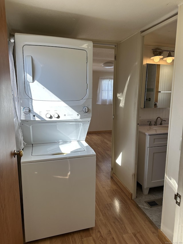 laundry room with visible vents, laundry area, stacked washer and clothes dryer, wood finished floors, and a sink