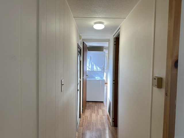 corridor featuring a textured ceiling, stacked washer and clothes dryer, and light wood-style flooring