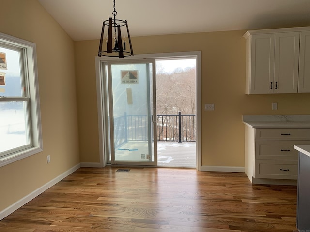 unfurnished dining area with light wood finished floors, visible vents, baseboards, and vaulted ceiling
