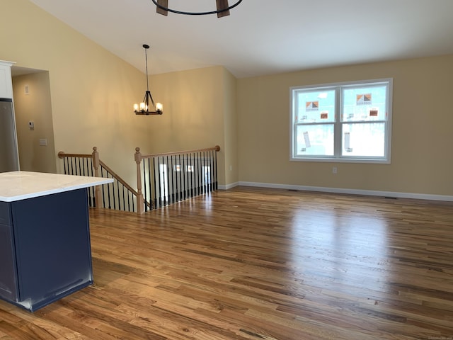 unfurnished living room featuring an inviting chandelier, vaulted ceiling, wood finished floors, and baseboards