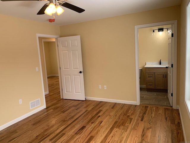 unfurnished bedroom featuring baseboards, visible vents, light wood-style flooring, a sink, and ensuite bathroom