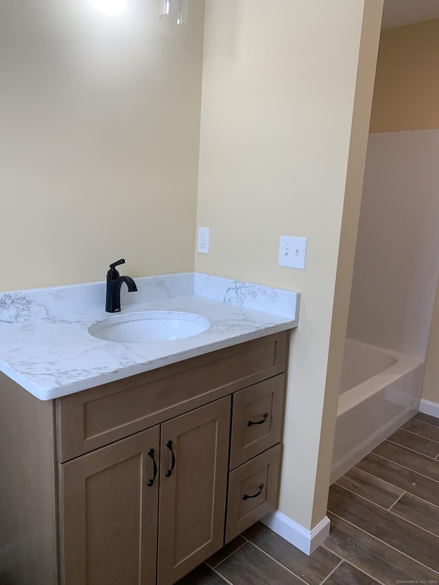 full bathroom with baseboards, a bathing tub, vanity, and wood finish floors