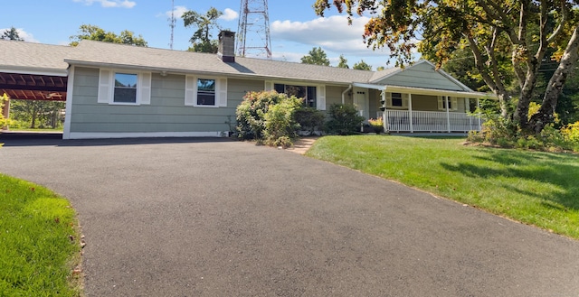 single story home with aphalt driveway, a front lawn, covered porch, and a chimney