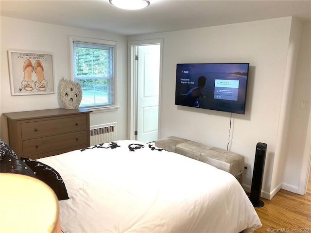 bedroom with radiator, wood finished floors, and baseboards