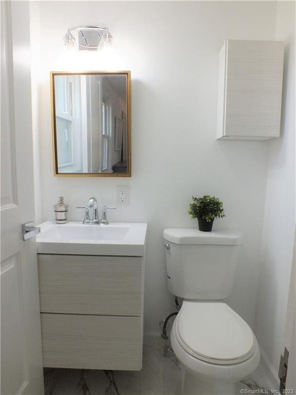 half bathroom with toilet, vanity, marble finish floor, and baseboards