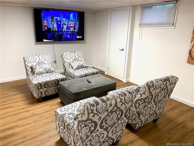 living area featuring a drop ceiling, baseboards, and wood finished floors