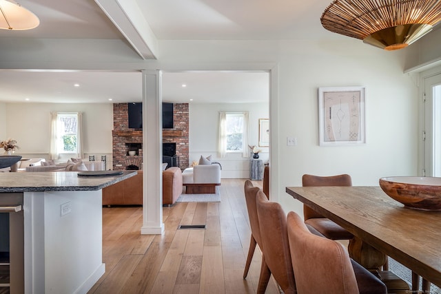 kitchen featuring a brick fireplace, light wood finished floors, decorative columns, and a healthy amount of sunlight