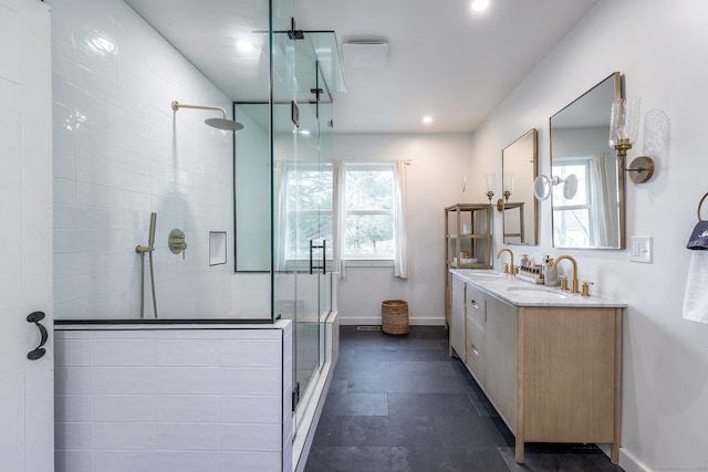 full bath featuring baseboards, a tile shower, double vanity, and a sink