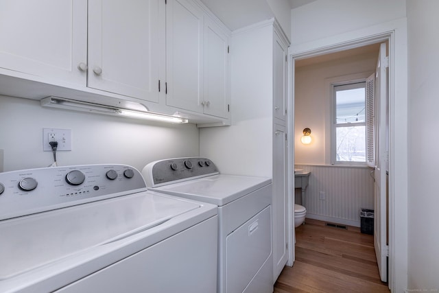 washroom with wood finished floors, separate washer and dryer, wainscoting, cabinet space, and visible vents