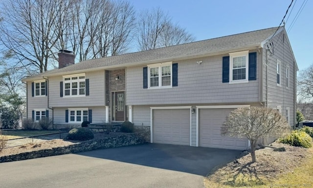 split foyer home with driveway, an attached garage, and a chimney