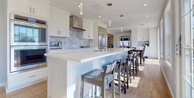 kitchen featuring a kitchen island with sink, a sink, decorative backsplash, appliances with stainless steel finishes, and wall chimney exhaust hood