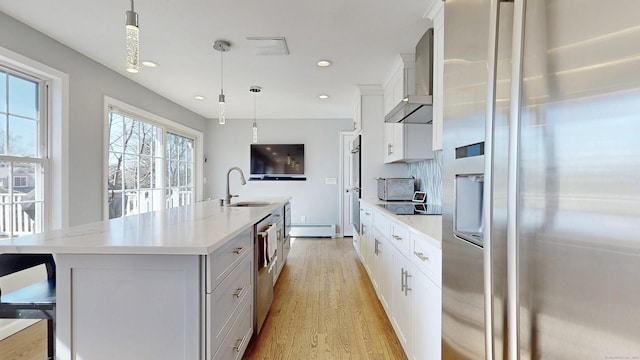 kitchen featuring a center island with sink, light wood-style flooring, appliances with stainless steel finishes, wall chimney exhaust hood, and a sink