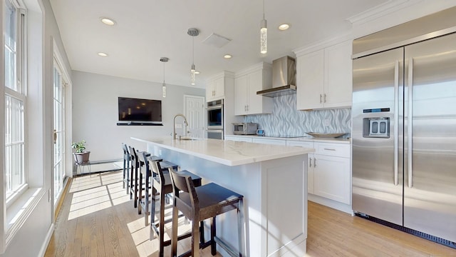 kitchen with light wood-style flooring, a sink, appliances with stainless steel finishes, wall chimney exhaust hood, and white cabinets